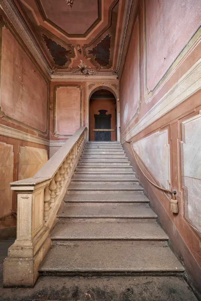 Scalone monumentale abbandonato di una villa storica con luce naturale e architettura d'epoca.