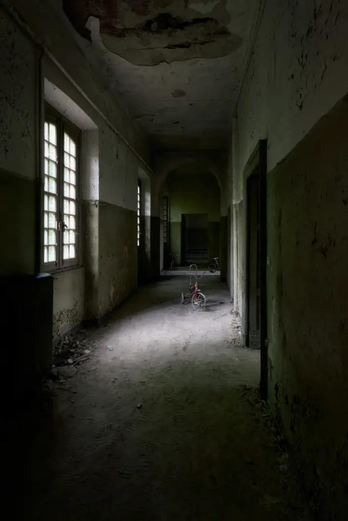 Corridoio di un manicomio abbandonato con un vecchio triciclo illuminato dalla luce naturale - fotografia fine art urbex